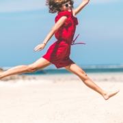 Woman in red dress jumping happy on the beach