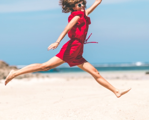 Frau im roten Kleid springt glücklich am Strand