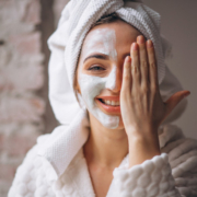Lächelnde Frau im Hausmantel mit einer Gesichtsmaske auf einer Seite ihres Gesichts