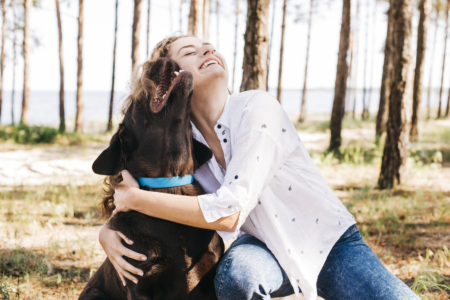 Smiling woman hugging dog in a forest
