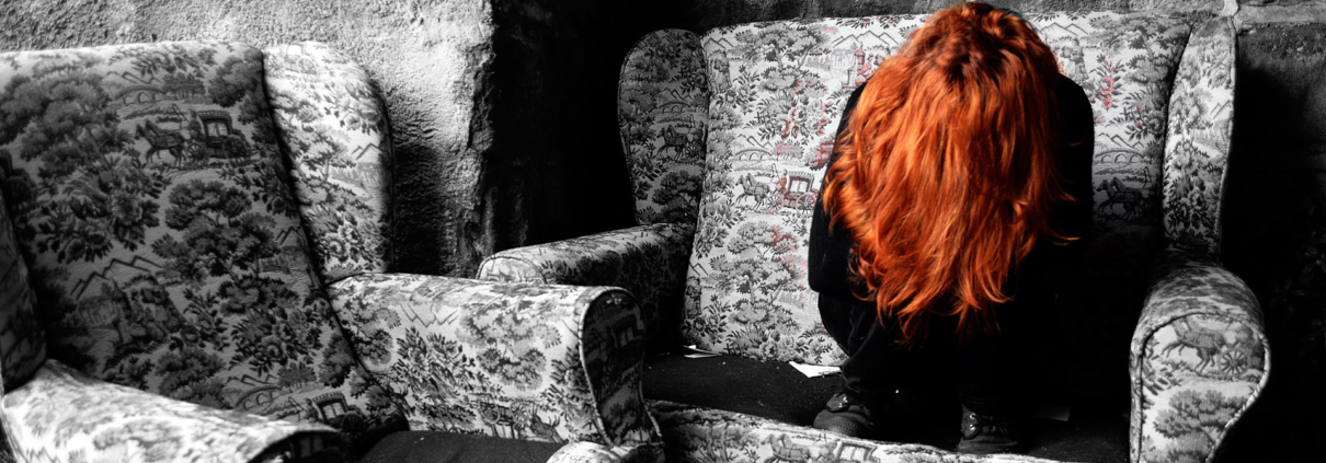 Femme dépressive aux cheveux roux, assise sur une chaise, effondrée.