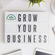 Bürotisch mit Computer, Telefon, Kaffeetasse, Notizbuch und einem Schild mit der Aufschrift "Grow your business".