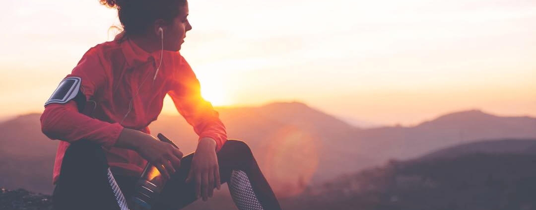Female runner sitting on mountain top gazing into the sunset