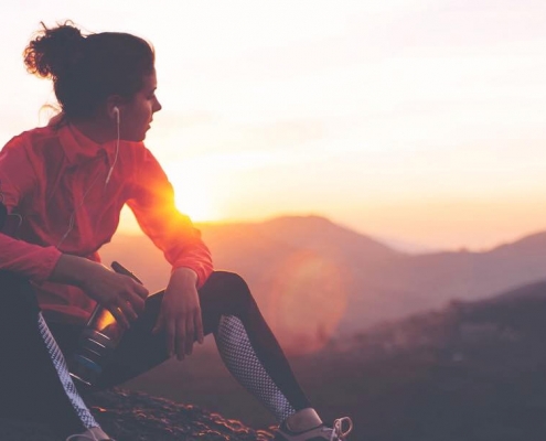 Läuferin sitzt auf einem Berggipfel und blickt in den Sonnenuntergang
