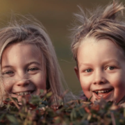 Zwei freche Kinder spähen über eine Hecke