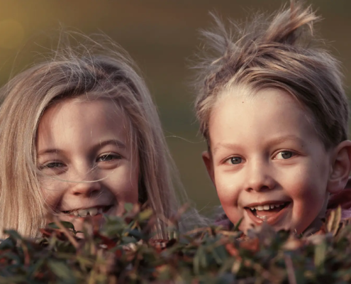 Zwei freche Kinder spähen über eine Hecke
