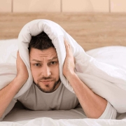 Man under the covers holding his ears