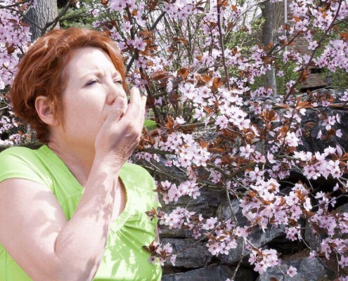 Woman sneezing in front of a tree with pink flowers