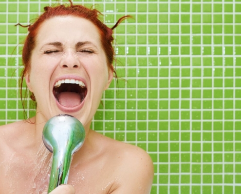 Happy woman singing into the shower head