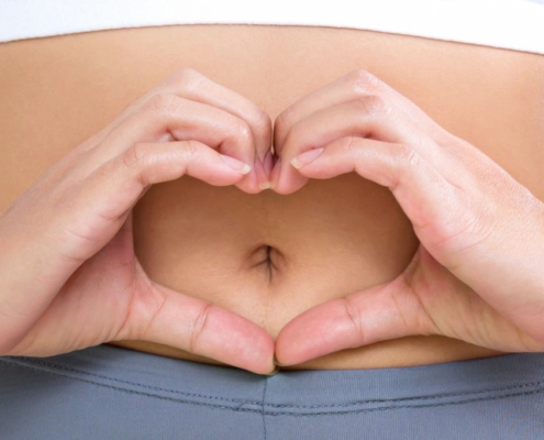 Woman making heart shape with her hands in front of her bellybutton