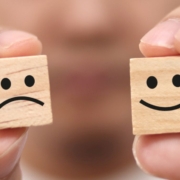 Hands holding happy and sad faced wooden cubes