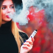 Junge hübsche Frau im Hintergrund bläst Vape Rauch auf einem roten Hintergrund