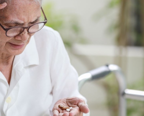 Ältere Person schaut verwirrt auf Tabletten in der Hand