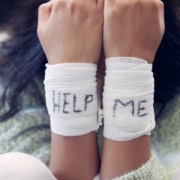 Frau mit Bandagen an den Handgelenken mit der Aufschrift HELP ME