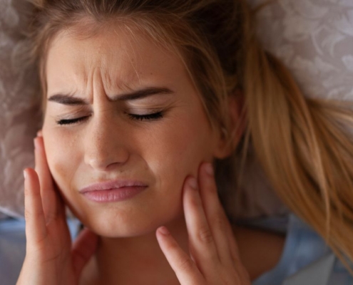 Woman holding her cheeks in pain after teeth grinding