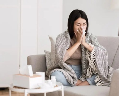 Woman with a clod on the sofa while blowing her nose