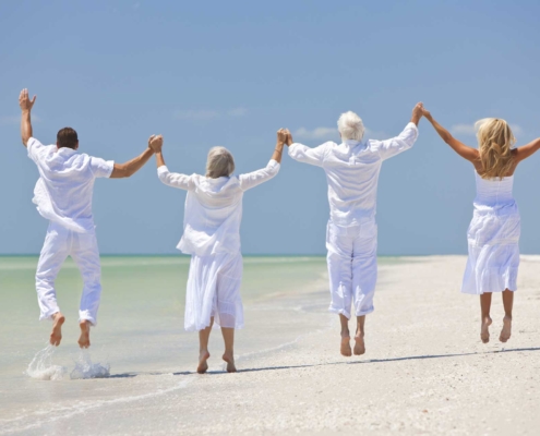 4 personas felices vestidas de blanco saltando en una playa exótica