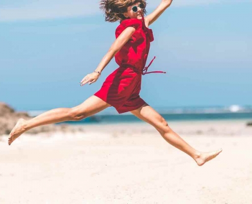 Mujer con vestido rojo saltando en la playa