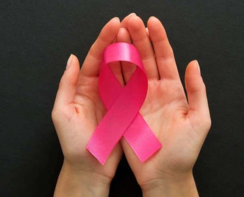 Manos femeninas sosteniendo un lazo rosa contra el cáncer