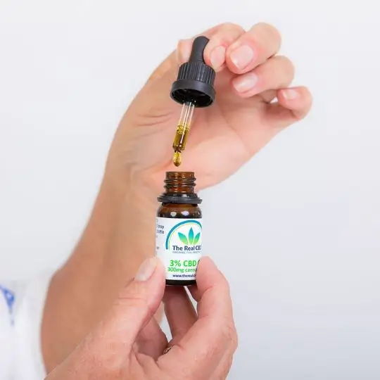 Mano con frasco abierto de aceite de CBD al 3% - - The Real CBD Marca