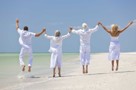 4 glückliche Menschen halten sich an den Händen und springen am Strand