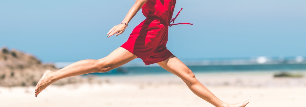 Frau im roten Kleid springt glücklich am Strand