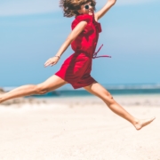 Frau im roten Kleid springt glücklich am Strand