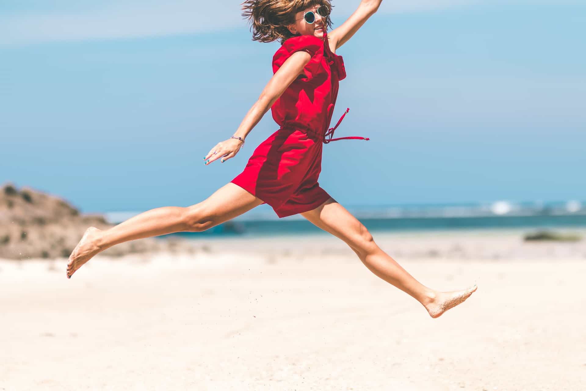 Frau im roten Kleid springt glücklich am Strand