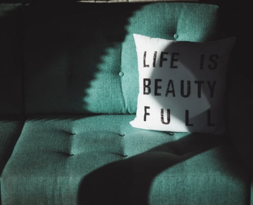 Canapé vert avec un oreiller blanc portant le texte "Life is beautiful" (la vie est belle)