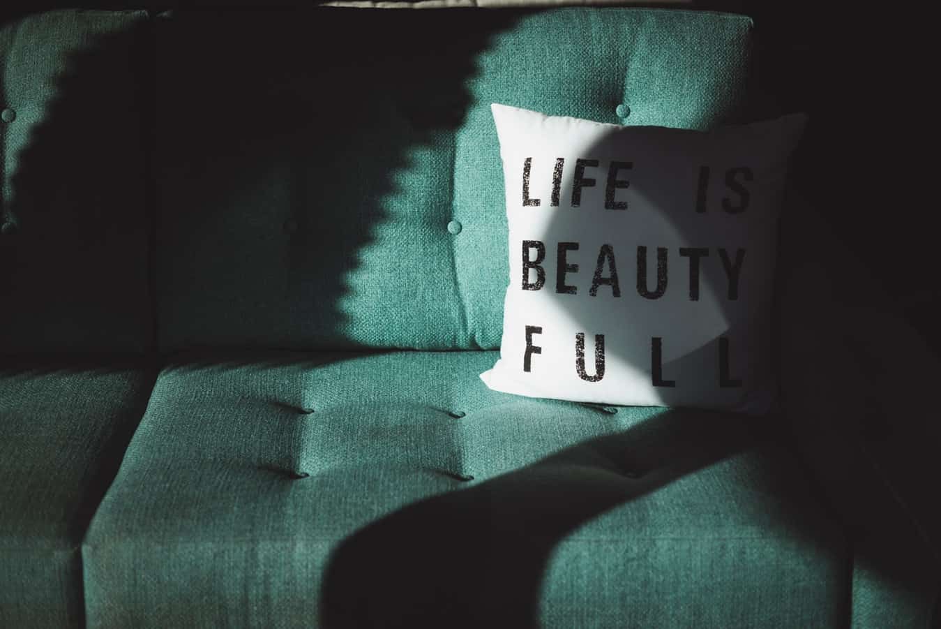 Canapé vert avec un oreiller blanc portant le texte "Life is beautiful" (la vie est belle)