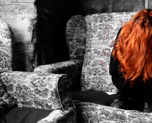 Depressed red haired woman sitting crumbled up in a chair