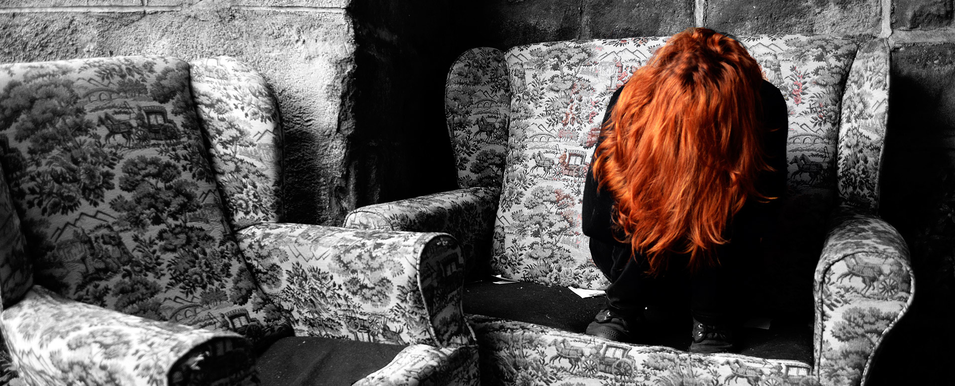 Depressed red haired woman sitting crumbled up in a chair