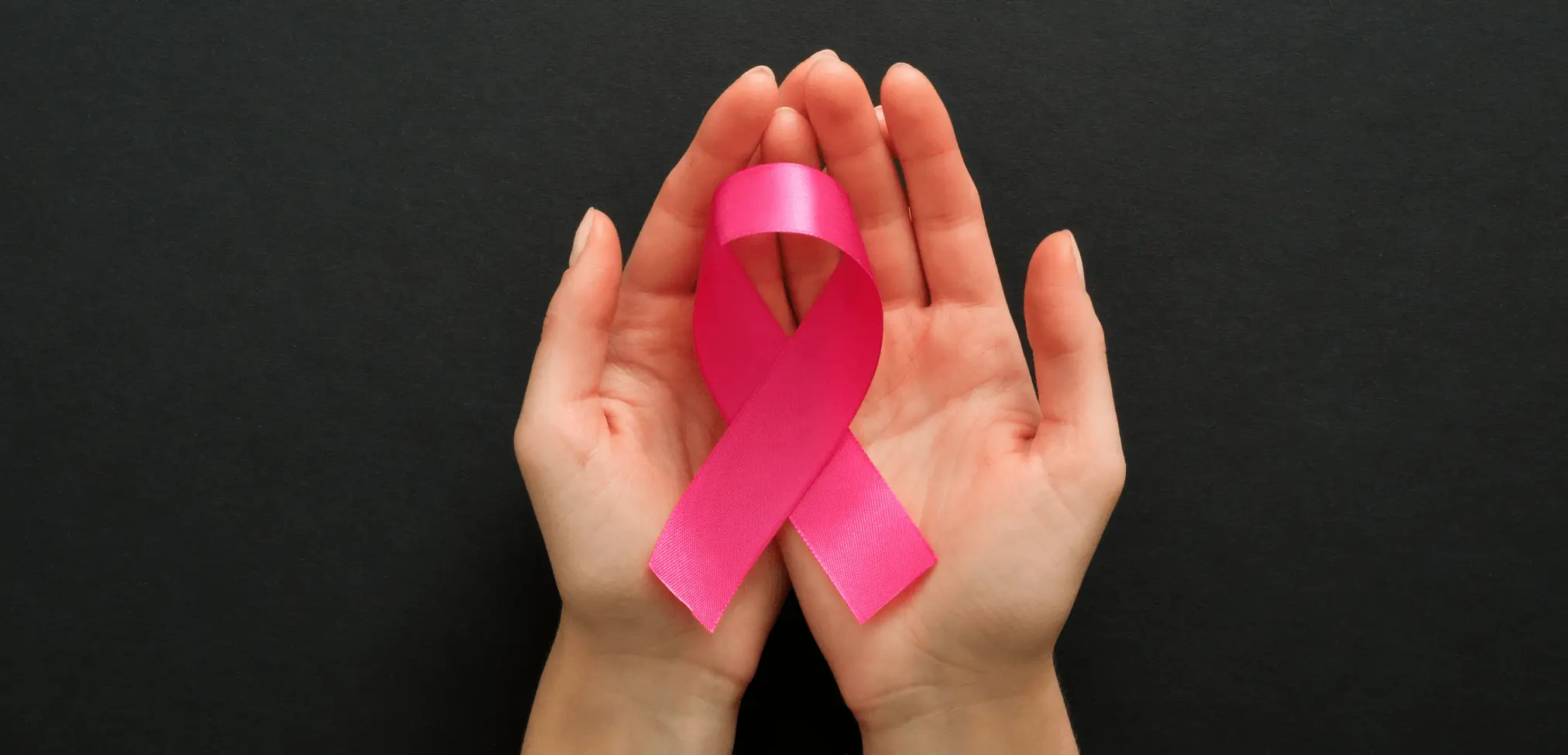 Hand holding a pink cancer ribbon