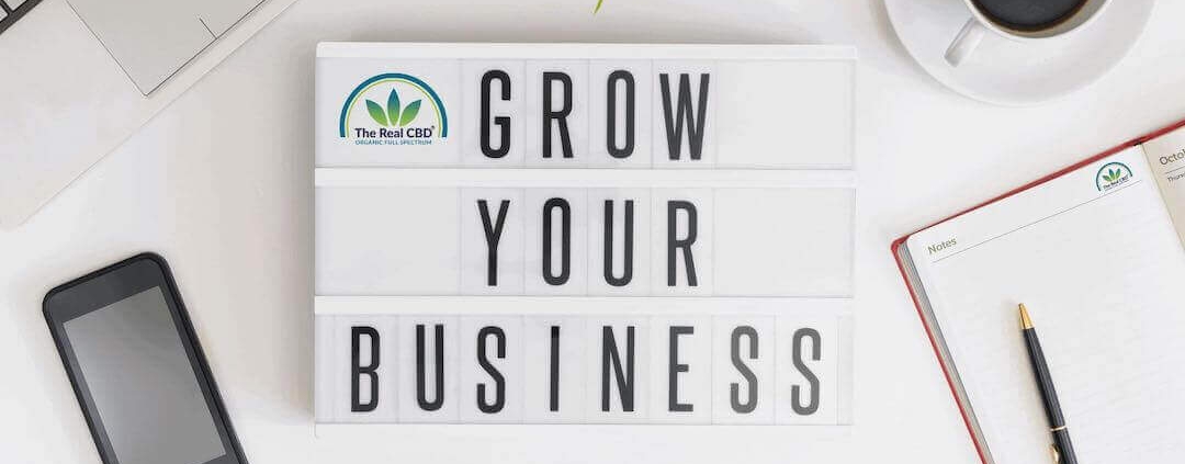 Office table with computer, phone coffee cup, notebook and a sign saying "Grow your business"