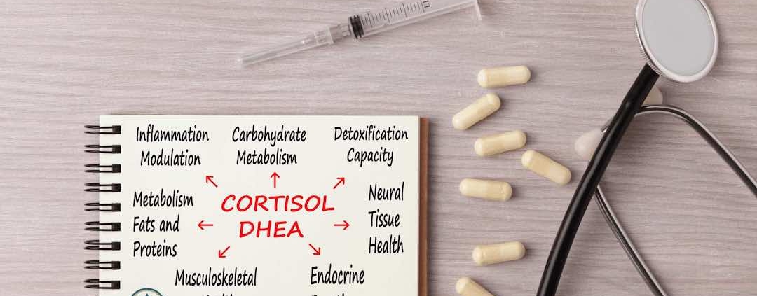 Cortisol DHEA auf einem Zettel, der auf einem Tisch mit Kapseln, einer Spritze und einem Stethoskop liegt