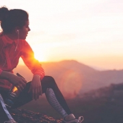 Läuferin sitzt auf einem Berggipfel und blickt in den Sonnenuntergang