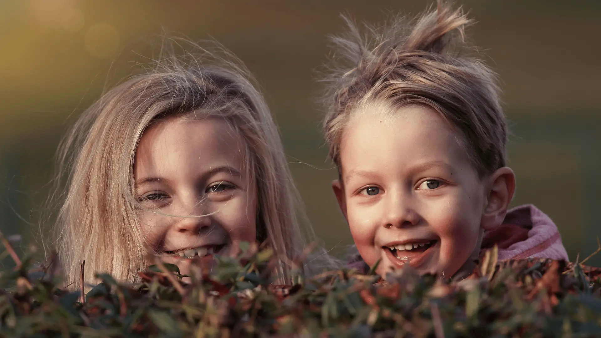 Zwei freche Kinder spähen über eine Hecke