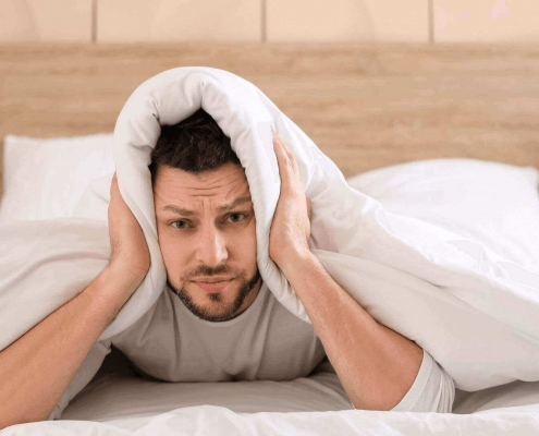 Man under the covers holding his ears