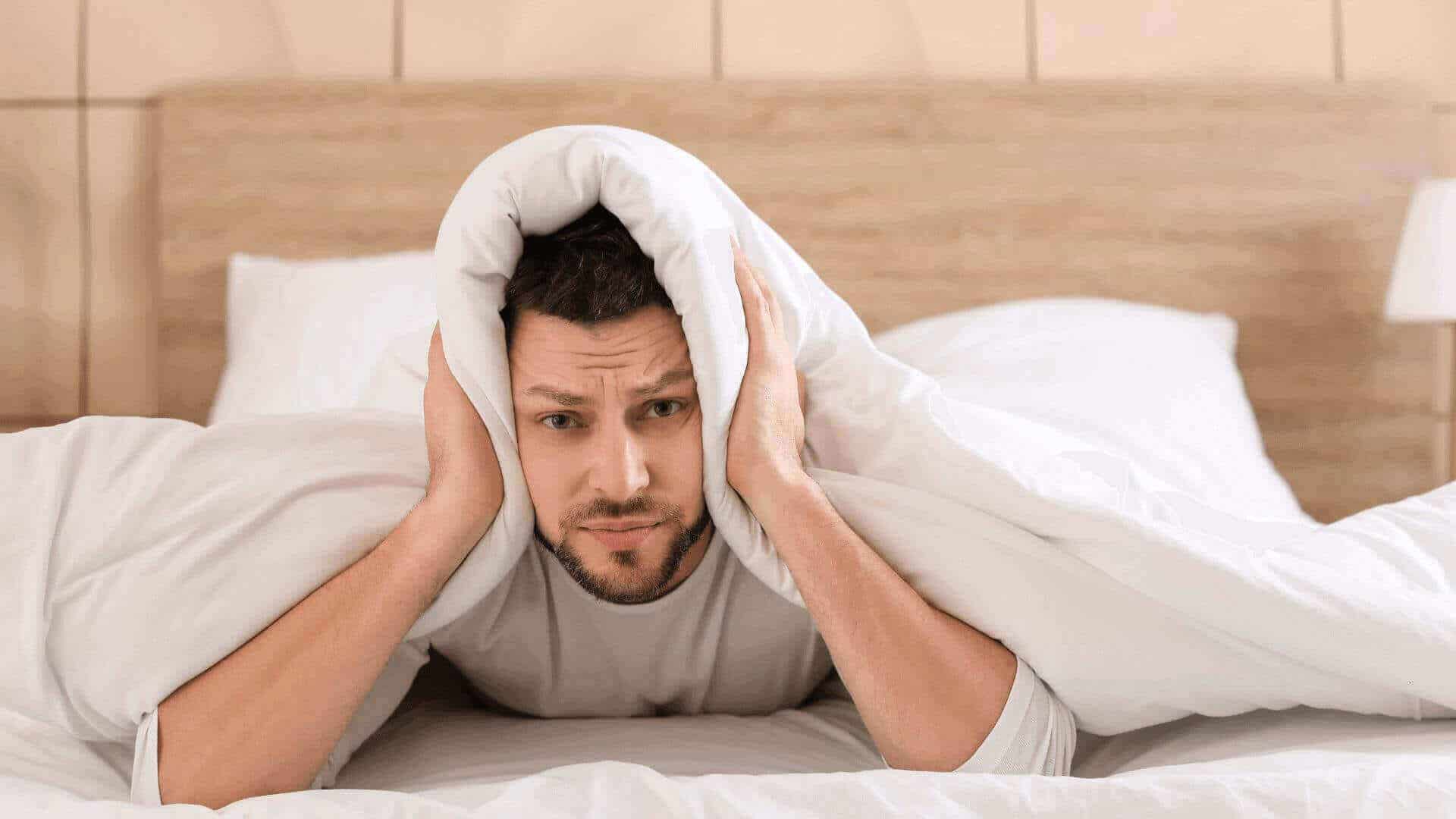 Man under the covers holding his ears