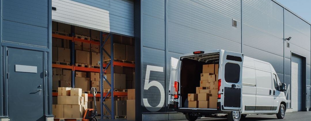 Camionnette blanche aux portes ouvertes devant un entrepôt