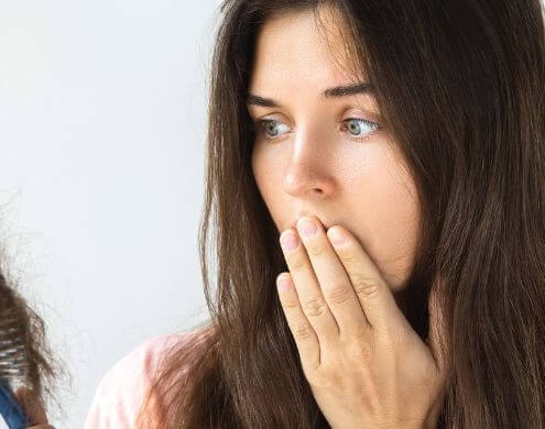 Femme regardant d'un air troublé une brosse à cheveux pleine de cheveux