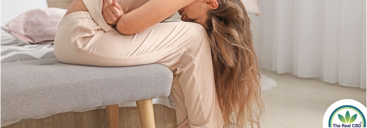 Woman with long hair sitting on a bed doubled over in pain