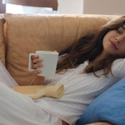 Woman laying on a sofa drinking from a white mug