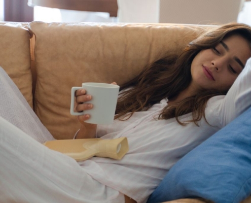 Woman laying on a sofa drinking from a white mug