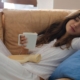 Woman laying on a sofa drinking from a white mug