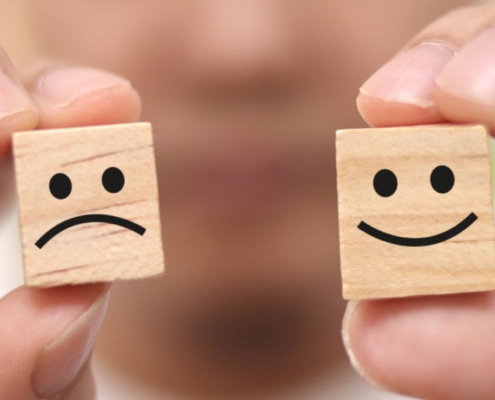 Hands holding happy and sad faced wooden cubes