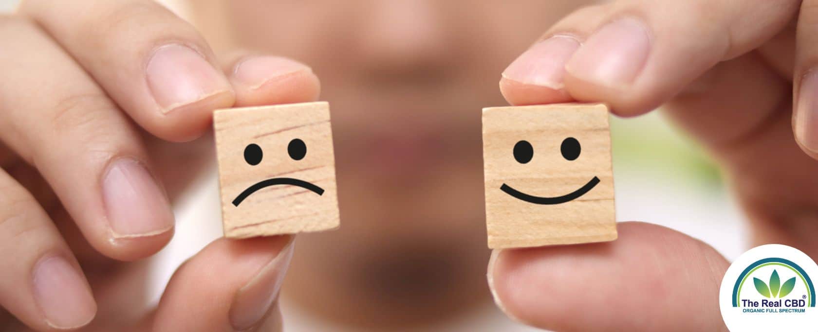 Hands holding happy and sad faced wooden cubes