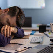 Mann schläft an einem Bürotisch mit mehreren Computern