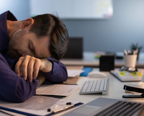 Mann schläft an einem Bürotisch mit mehreren Computern