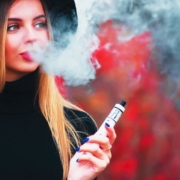 Jeune femme jolie de dos soufflant de la fumée de vapotage sur fond rouge